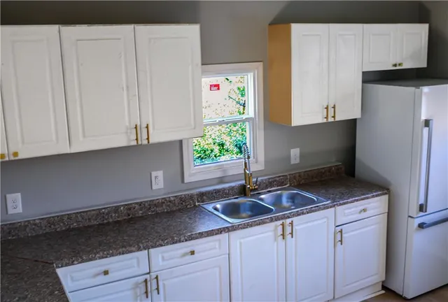 a kitchen with granite countertop a sink a stove a refrigerator and white cabinets