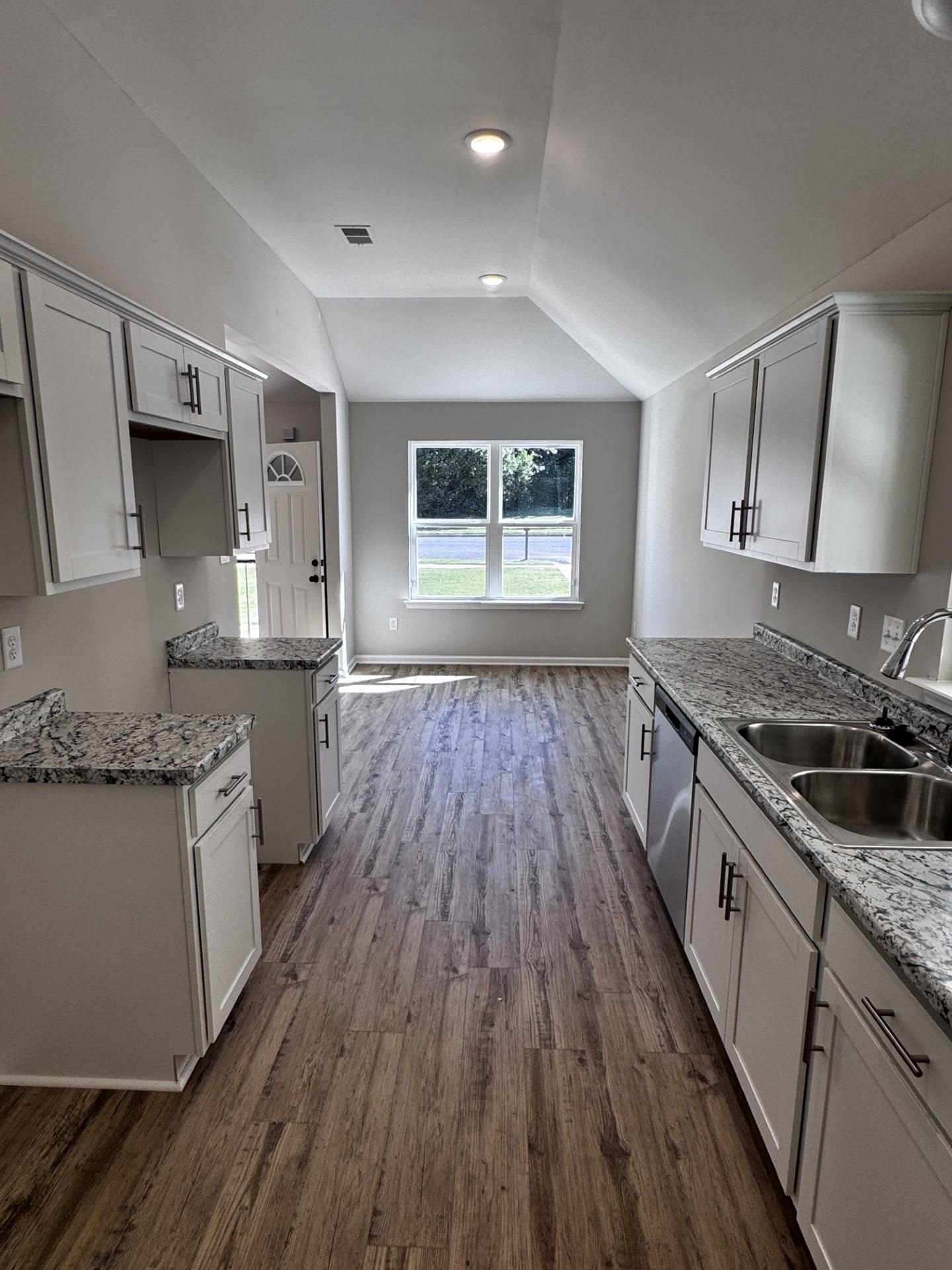5243 Zodiac Road Memphis, TN 38118 - Photo 8 of 10 Kitchen featuring vaulted ceiling, dark wood-type flooring, stainless steel dishwasher, light stone countertops, and white cabinetry