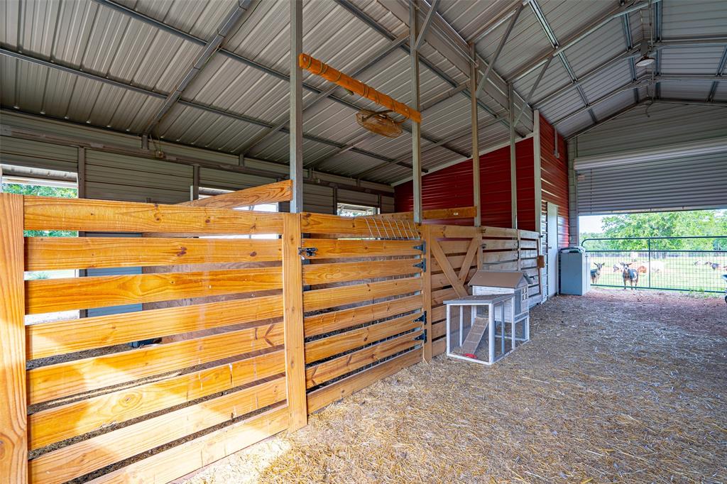 1920 Meander Road Granbury, TX 76049 - Photo 31 of 40 Spacious barn interior featuring a metal roof structure, wood fencing and gate, red corrugated metal siding, and a large roll-up door