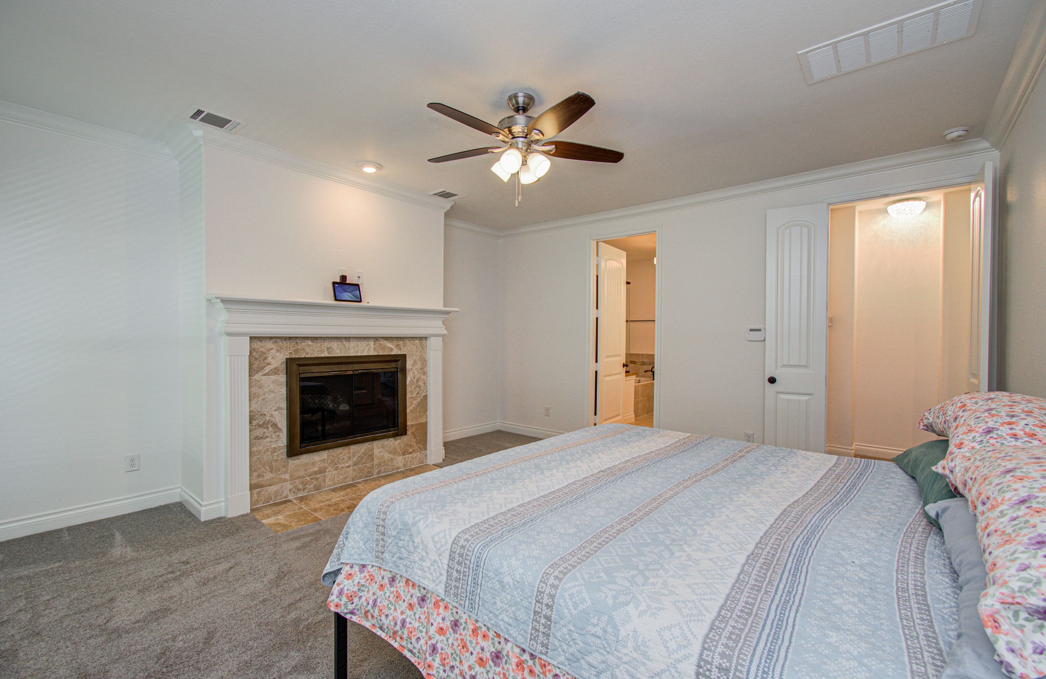 6621 North Main Street Houston, TX 77009 - Photo 16 of 41 This cozy bedroom features a built-in fireplace with a tiled surround, a ceiling fan, and an en-suite bathroom. The room has soft carpeting and neutral walls, offering a warm and inviting atmosphere.
