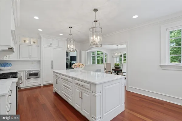 a large white kitchen with a large counter top space a sink stainless steel appliances and cabinets