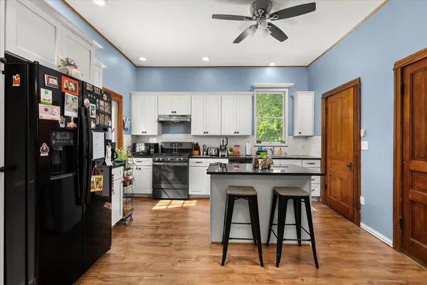 a kitchen with stainless steel appliances granite countertop a refrigerator a sink dishwasher a stove and a dining table with wooden floor