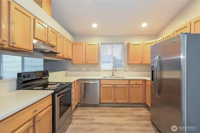 a kitchen with stainless steel appliances granite countertop a stove a sink dishwasher a refrigerator and cabinets with wooden floor