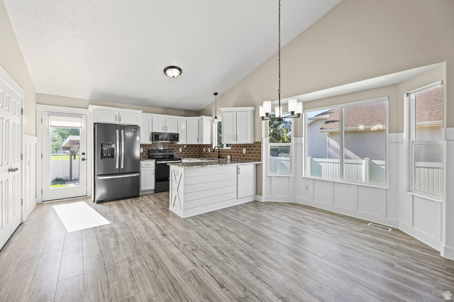 5525 Hampton Way Stansbury Park, UT 84074 - Photo 5 of 35 Open-concept kitchen and dining area featuring vaulted ceilings, wood-finish flooring, white cabinetry, and a granite-topped island with shiplap detail