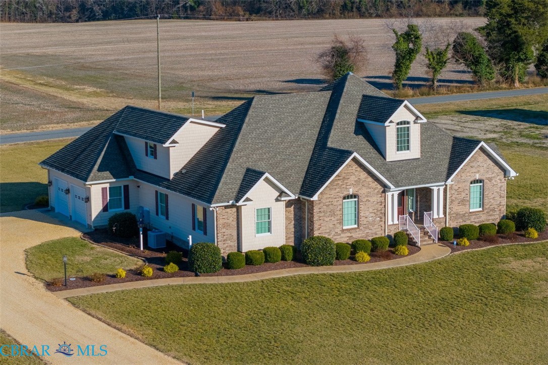 View of front facade featuring a front lawn, a porch, a shingled roof, and driveway