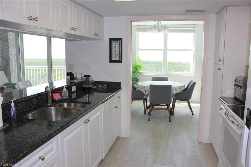 6573 Marissa Loop, Unit 902 Naples, FL 34108 - Photo 6 of 26 a kitchen with granite countertop a sink and white cabinets with wooden floor