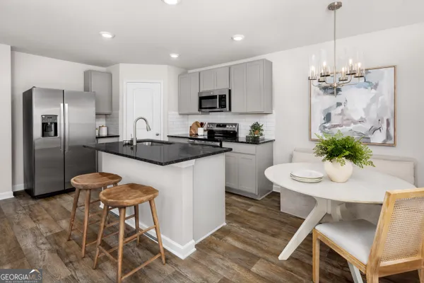 a kitchen with stainless steel appliances kitchen island granite countertop a dining table chairs and a refrigerator