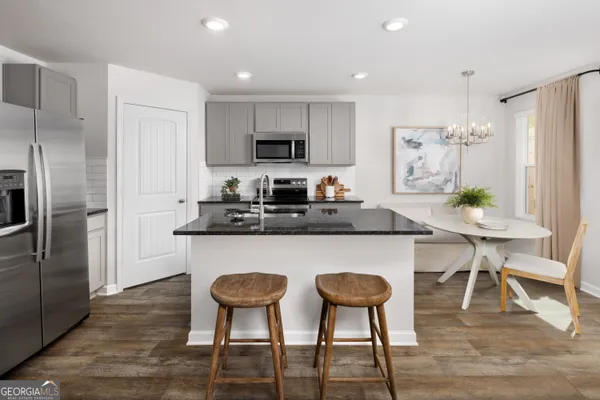 a kitchen with stainless steel appliances granite countertop a dining table chairs refrigerator and sink