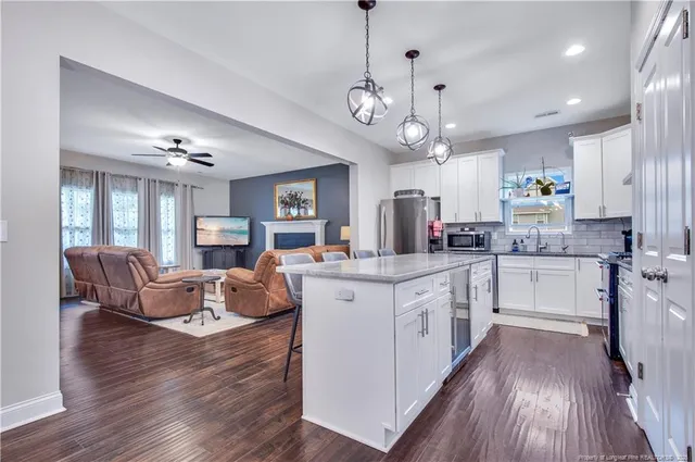 a open kitchen with stainless steel appliances granite countertop a refrigerator a stove top oven a dining table and chairs with wooden floor