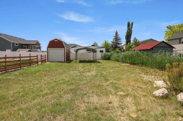 3636 West 910 South Syracuse, UT 84075 - Photo 68 of 70 Expansive grassy yard featuring a red barn-style shed with a white garage door, a metal carport, and a rustic wood fence