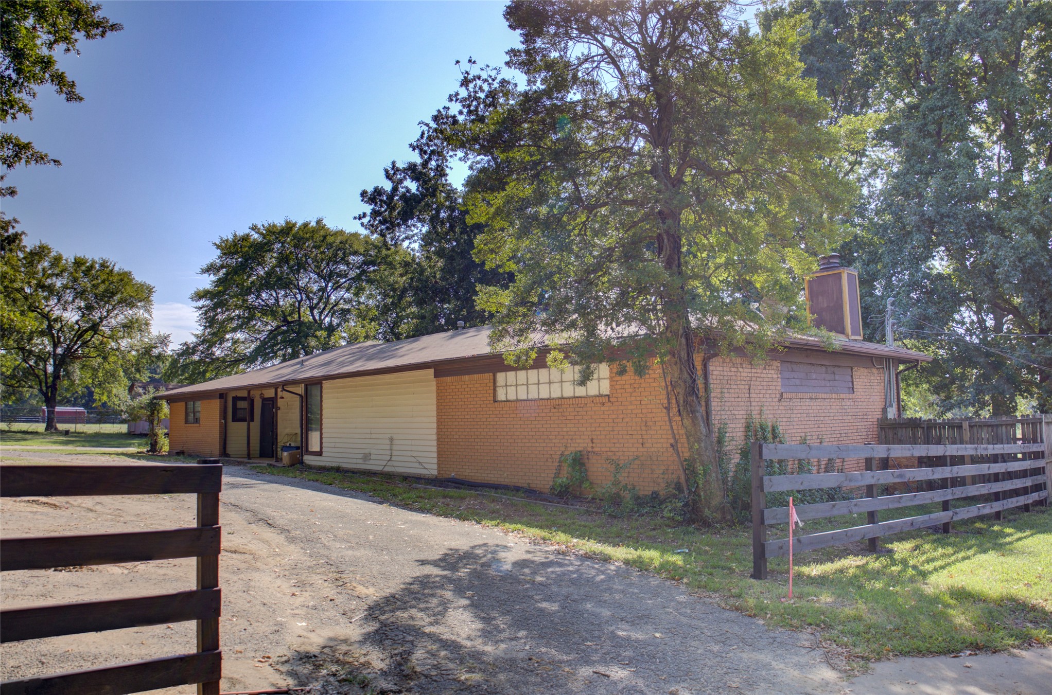 12420 South Garnett Road Broken Arrow, OK 74011 - Photo 3 of 44 Brick and siding exterior with a wood fence, gravel driveway, and mature trees
