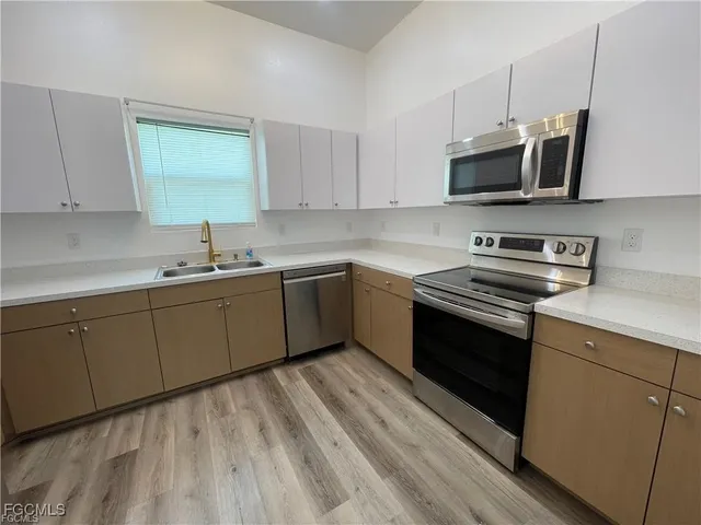 a kitchen with stainless steel appliances a sink dishwasher stove and microwave with wooden floor