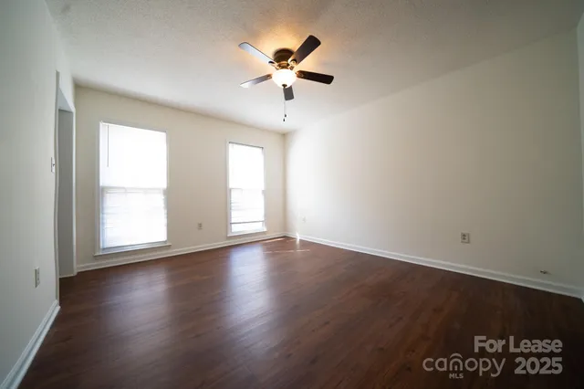 an empty room with wooden floor chandelier fan and windows