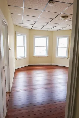 an empty room with wooden floor and windows with curtains