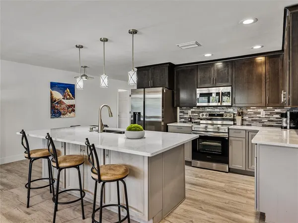 a kitchen with stainless steel appliances kitchen island granite countertop a dining table chairs refrigerator and sink