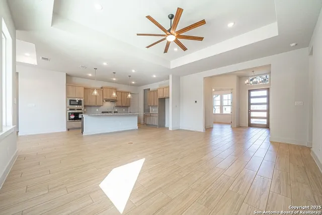 a view of an empty room and kitchen with wooden floor