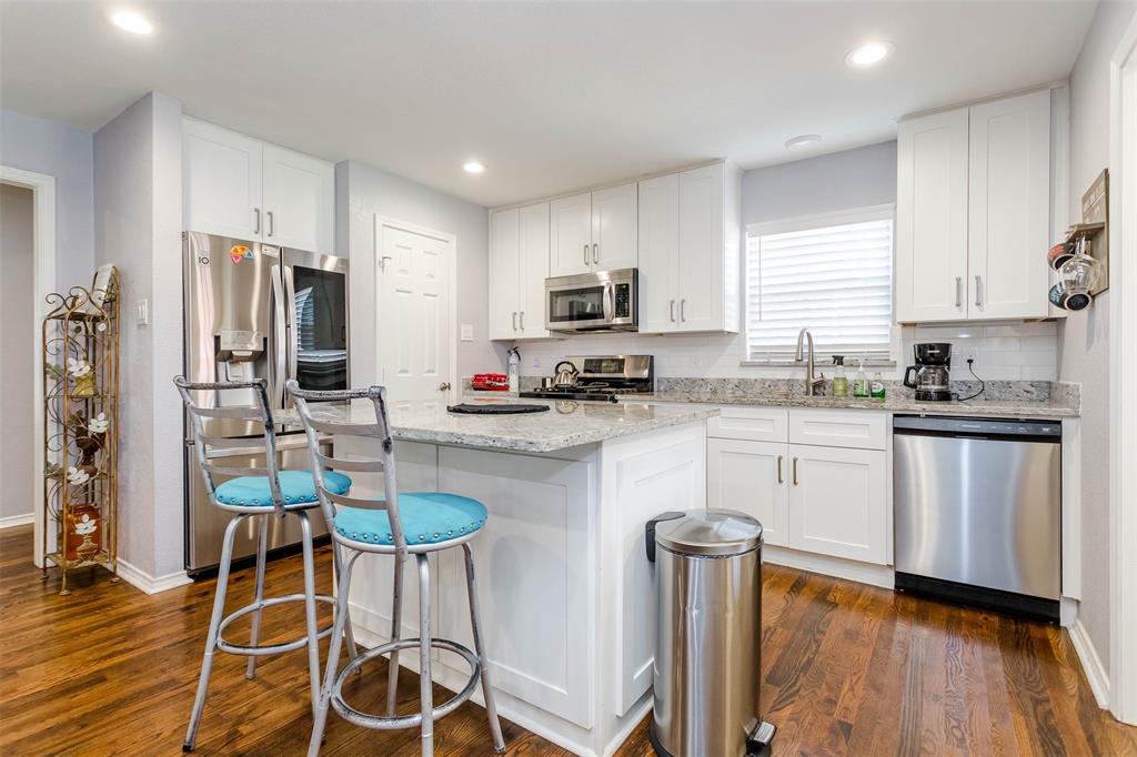 a kitchen with stainless steel appliances granite countertop a refrigerator a stove a sink dishwasher a stove and white cabinets with wooden floor