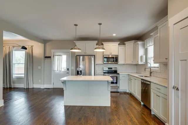 a kitchen with stainless steel appliances granite countertop a refrigerator a sink dishwasher a stove and white countertops with wooden floor