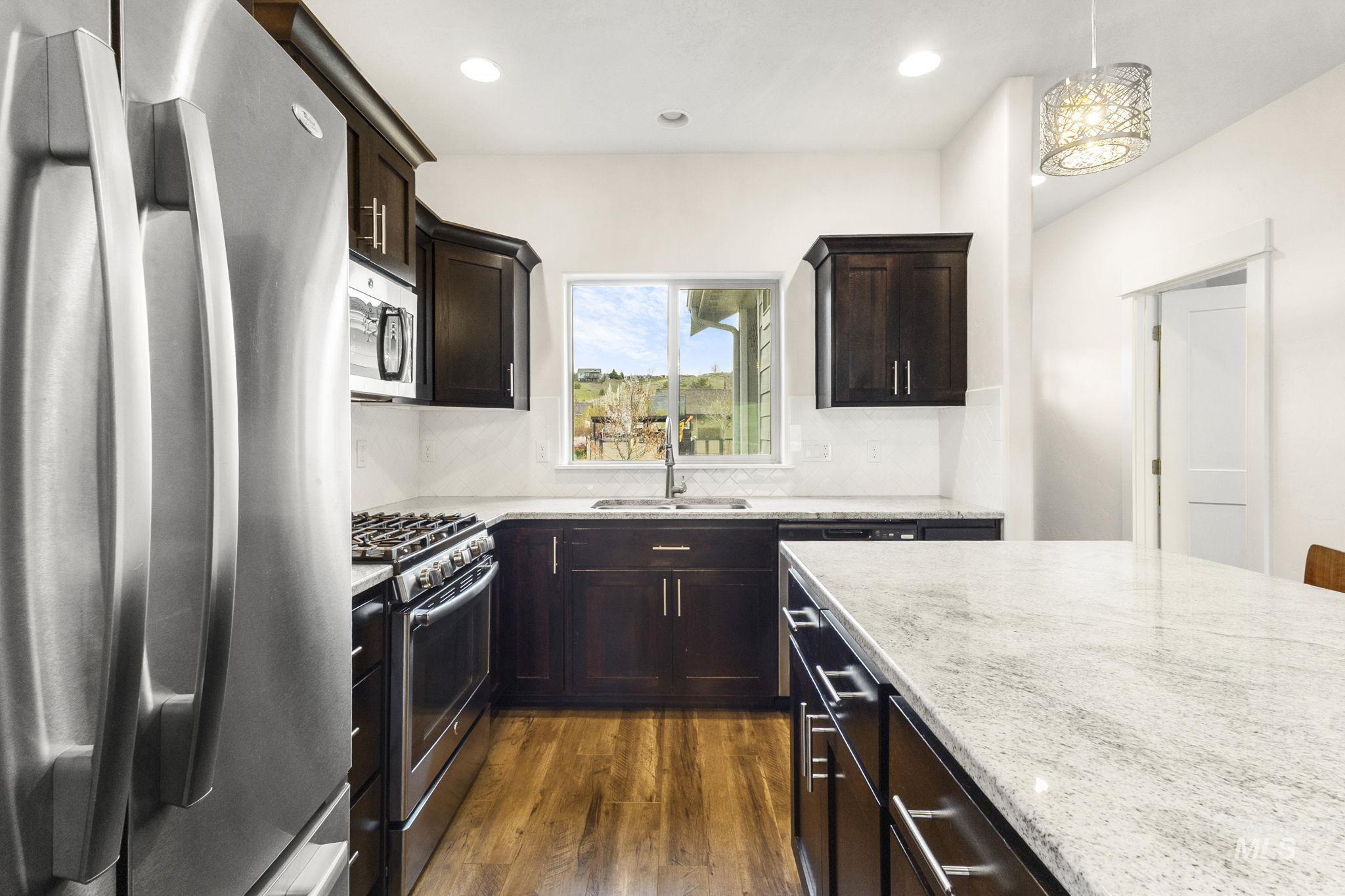 18293 North Streams Edge Way Boise, ID 83714 - Photo 4 of 50 Kitchen with stainless steel appliances, dark wood finish cabinetry, light stone counters, dark wood-type flooring, and decorative light fixtures