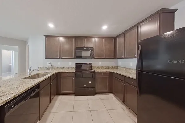 a large kitchen with stainless steel appliances granite countertop a sink and dishwasher a refrigerator with wooden cabinets