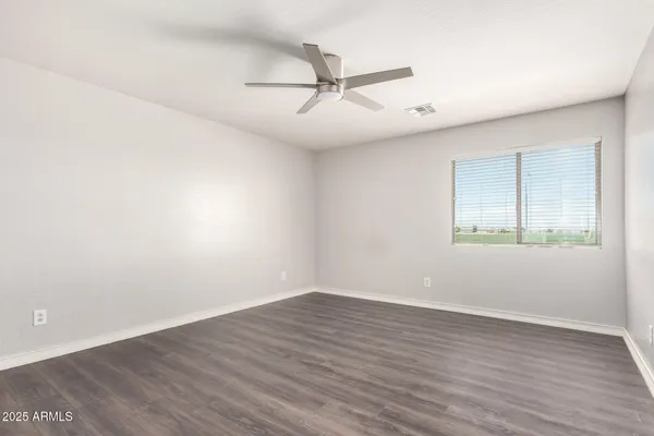 an empty room with wooden floor fan and windows