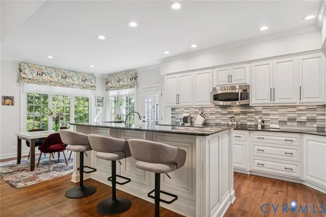 a kitchen with stainless steel appliances granite countertop a stove top oven a sink dishwasher a dining table and chairs with wooden floor