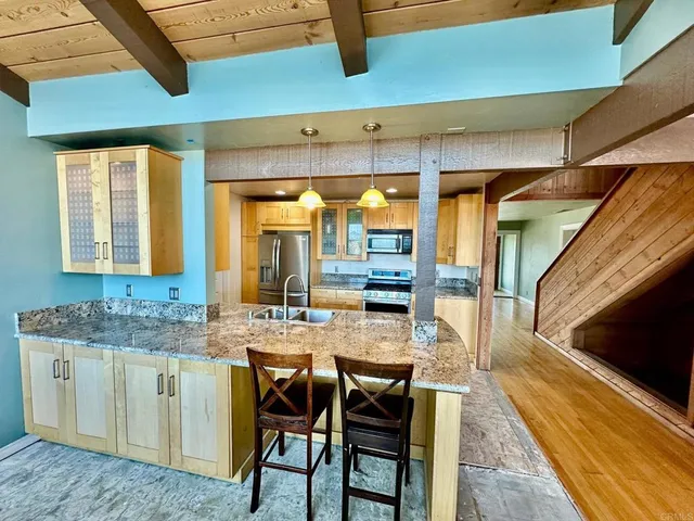 a dining hall with stainless steel appliances kitchen island granite countertop a table chairs in it and wooden floors