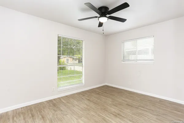 an empty room with wooden floor ceiling fan and windows