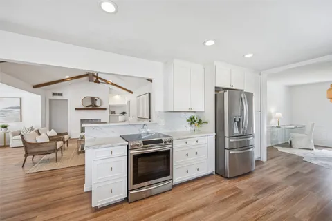 a kitchen with stainless steel appliances a stove a refrigerator and white cabinets with wooden floor