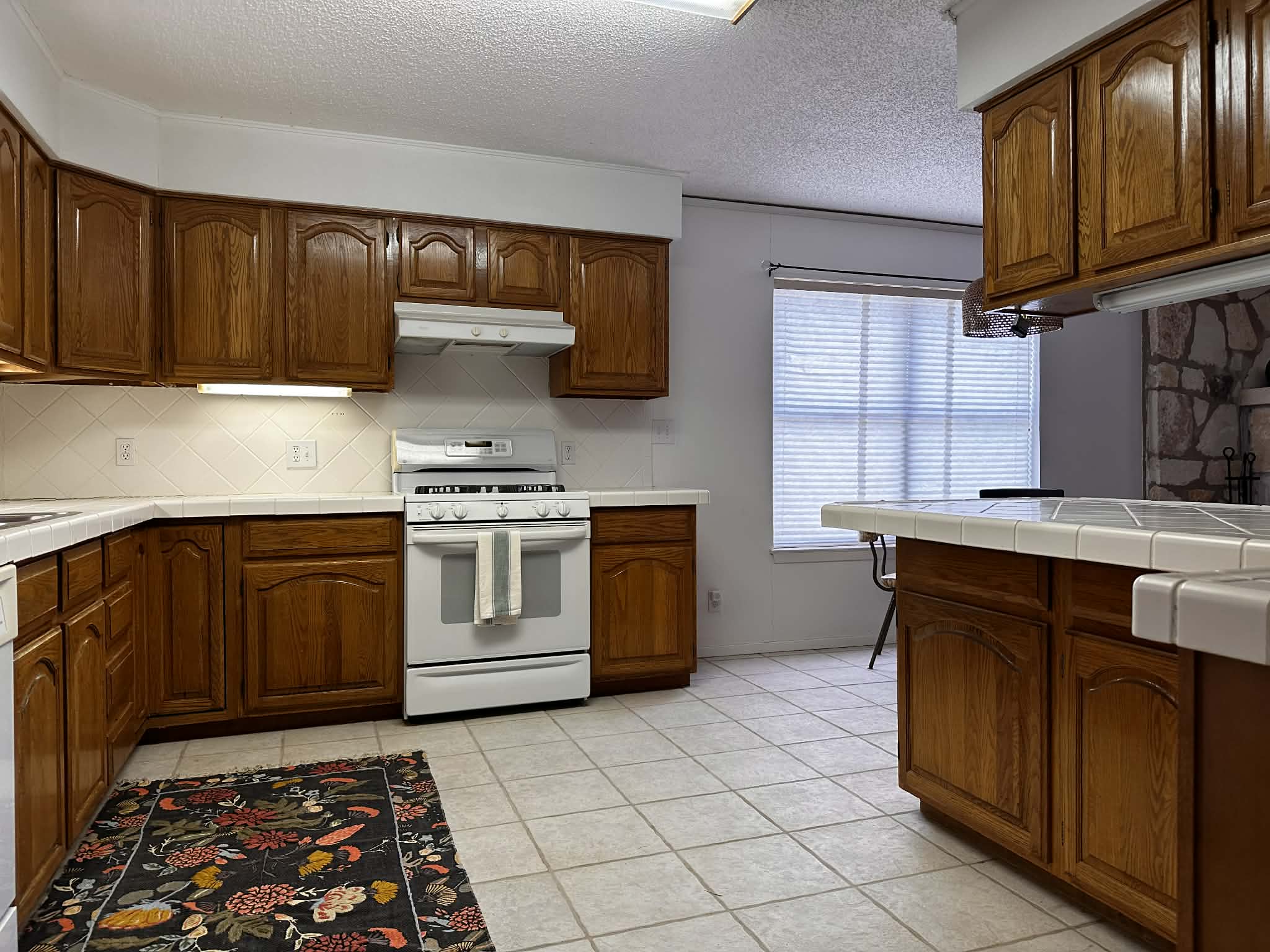 810 Kc 271 Junction Junction, TX 76849 - Photo 19 of 20 Kitchen featuring tile counters, white gas stove, a textured ceiling, light tile patterned flooring, and wood finish cabinetry