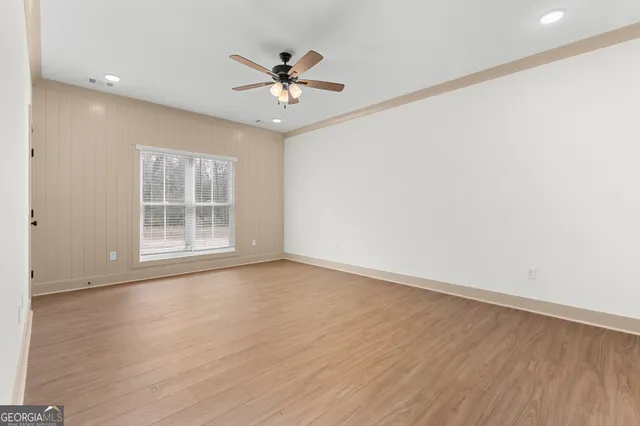 an empty room with wooden floor chandelier fan and windows
