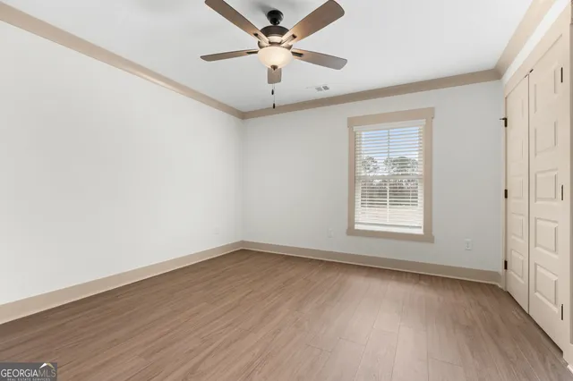 an empty room with wooden floor ceiling fan and windows