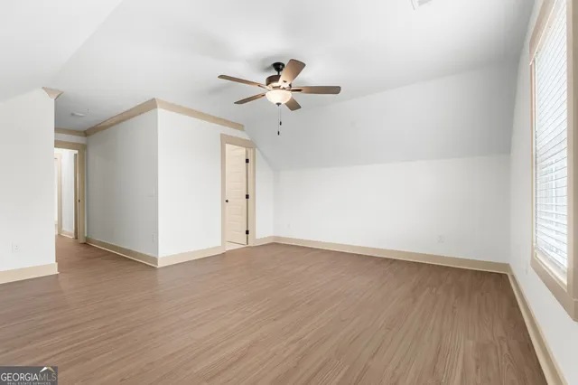 an empty room with wooden floor ceiling fan and windows