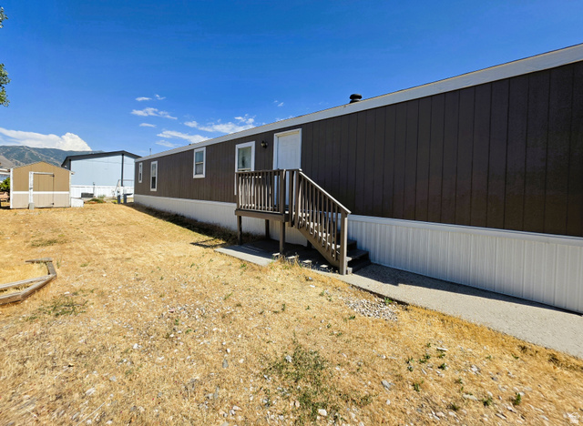 1604 180 East Tooele, UT 84074 - Photo 2 of 16 Gray exterior siding with white trim, featuring a wooden deck with stairs to the entrance
