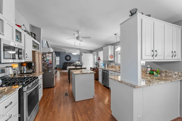 a kitchen with stainless steel appliances kitchen island granite countertop a refrigerator a stove top oven a sink dishwasher and white cabinets with wooden floor