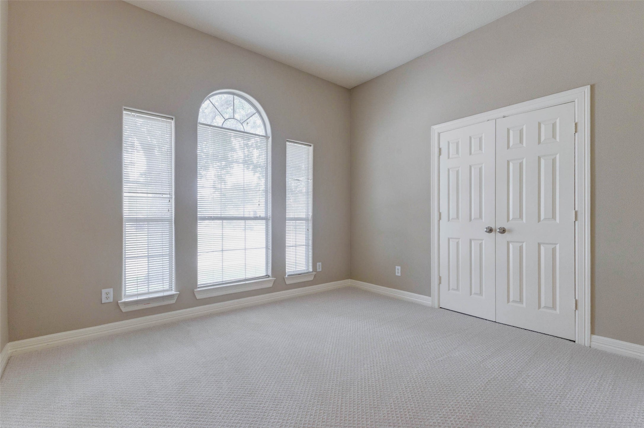 2718 Ridgeglen Lane Houston, TX 77082 - Photo 11 of 26 Comfortable bedroom with soft carpet, neutral wall color, high ceiling and a striking arched center window flanked by two narrow side windows. The window arrangement adds architectural character and natural light, while double closet doors provide built-in storage. White trim and simple finishes create a clean, move-in-ready space that can function beautifully as a bedroom, guest room or office.