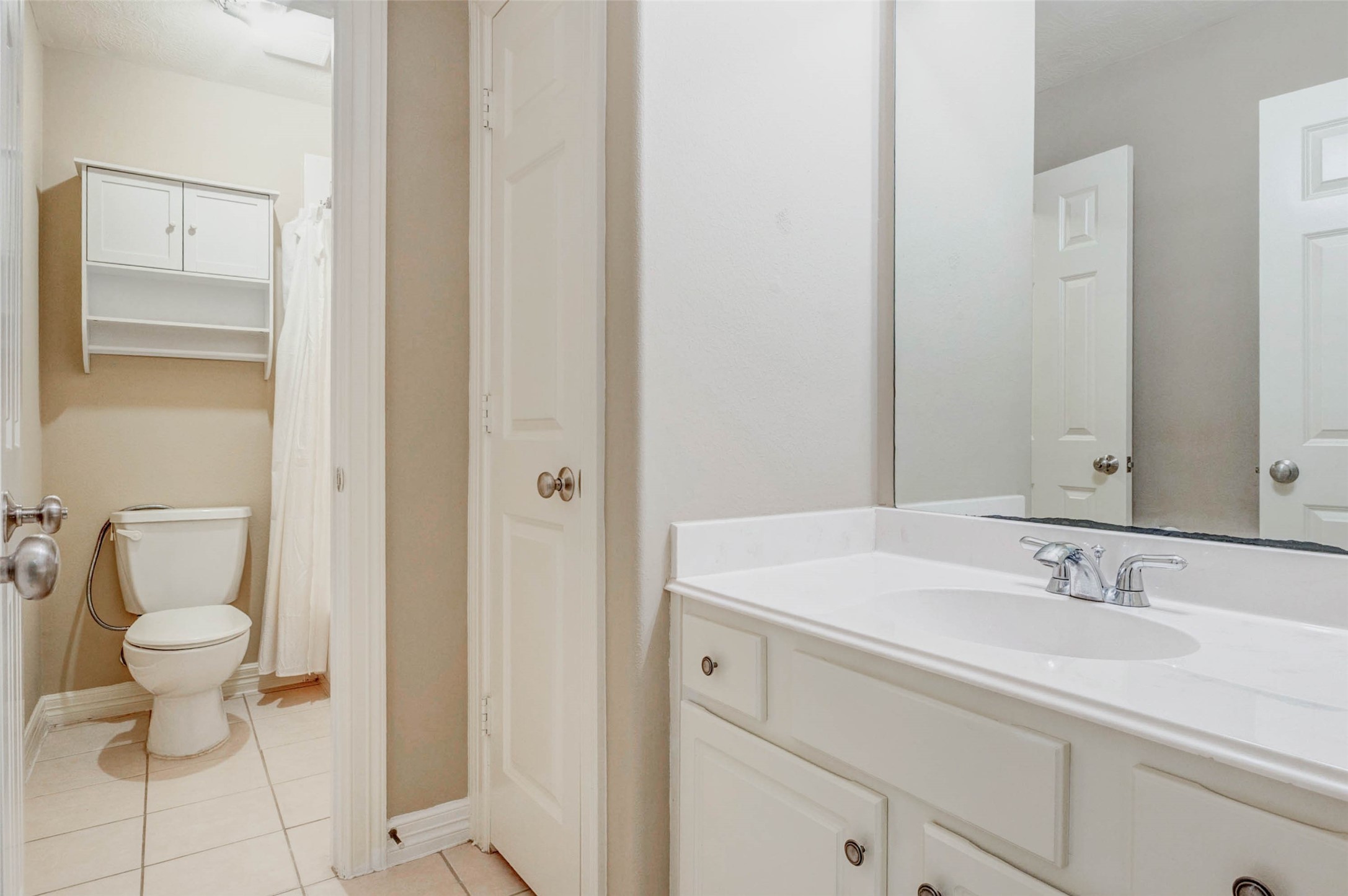 2718 Ridgeglen Lane Houston, TX 77082 - Photo 13 of 26 Secondary bathroom with a clean white vanity, large mirror, chrome faucet and neutral tile flooring. The adjoining bath area includes a toilet, tub/shower with curtain and built-in wall storage above, creating practical space for linens and essentials. Neutral finishes and white cabinetry keep the room bright and functional, offering an easy-to-maintain bath for guests or secondary bedrooms.