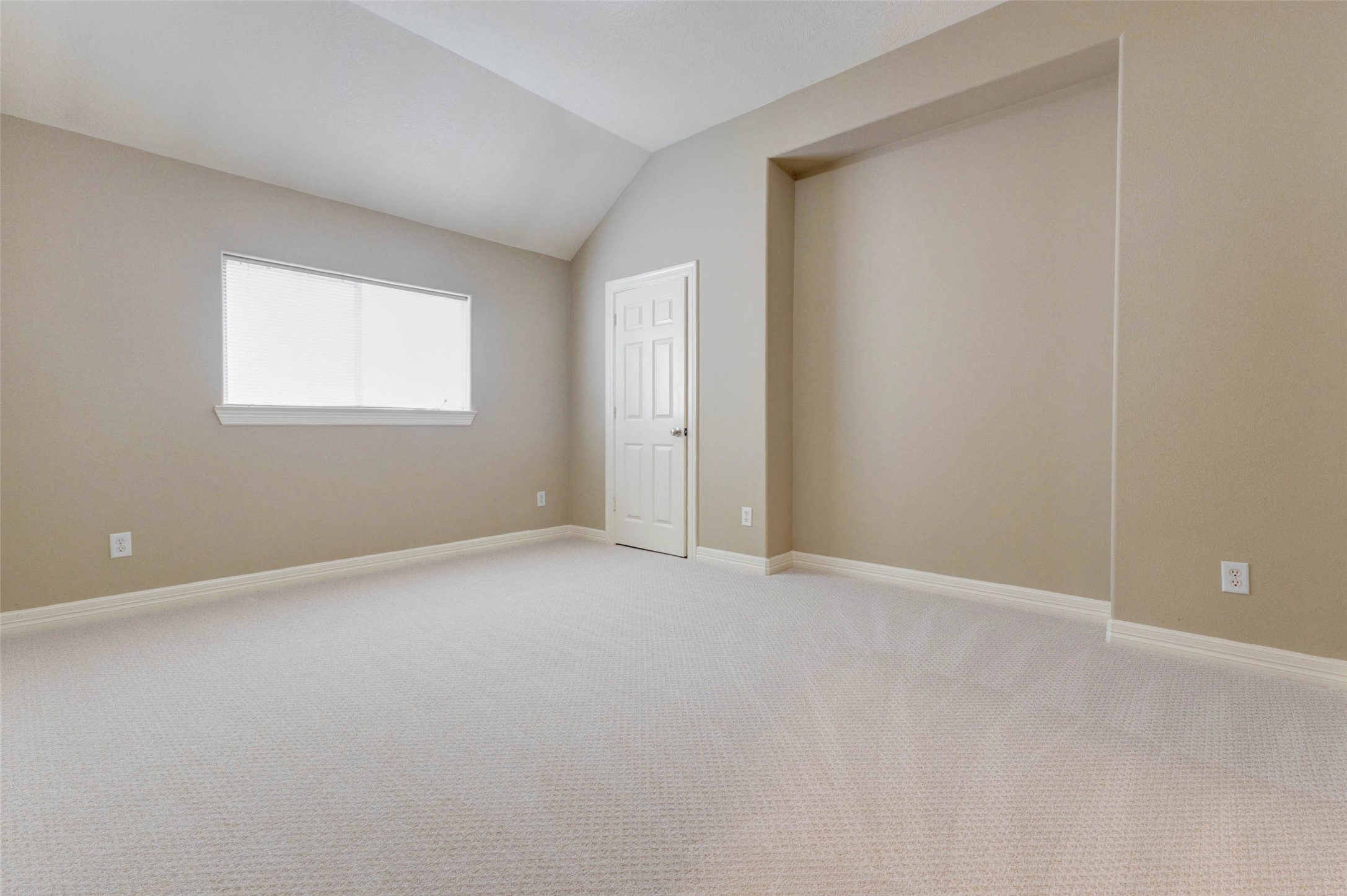 2718 Ridgeglen Lane Houston, TX 77082 - Photo 14 of 26 Spacious bedroom with soft carpet, neutral walls, vaulted ceiling, white trim and a wide horizontal window for natural light. The room offers plenty of open floor space and a recessed wall niche that could work well for a dresser, reading corner, desk or media setup. A nearby door provides closet access, while the calm color palette makes the space easy to personalize.