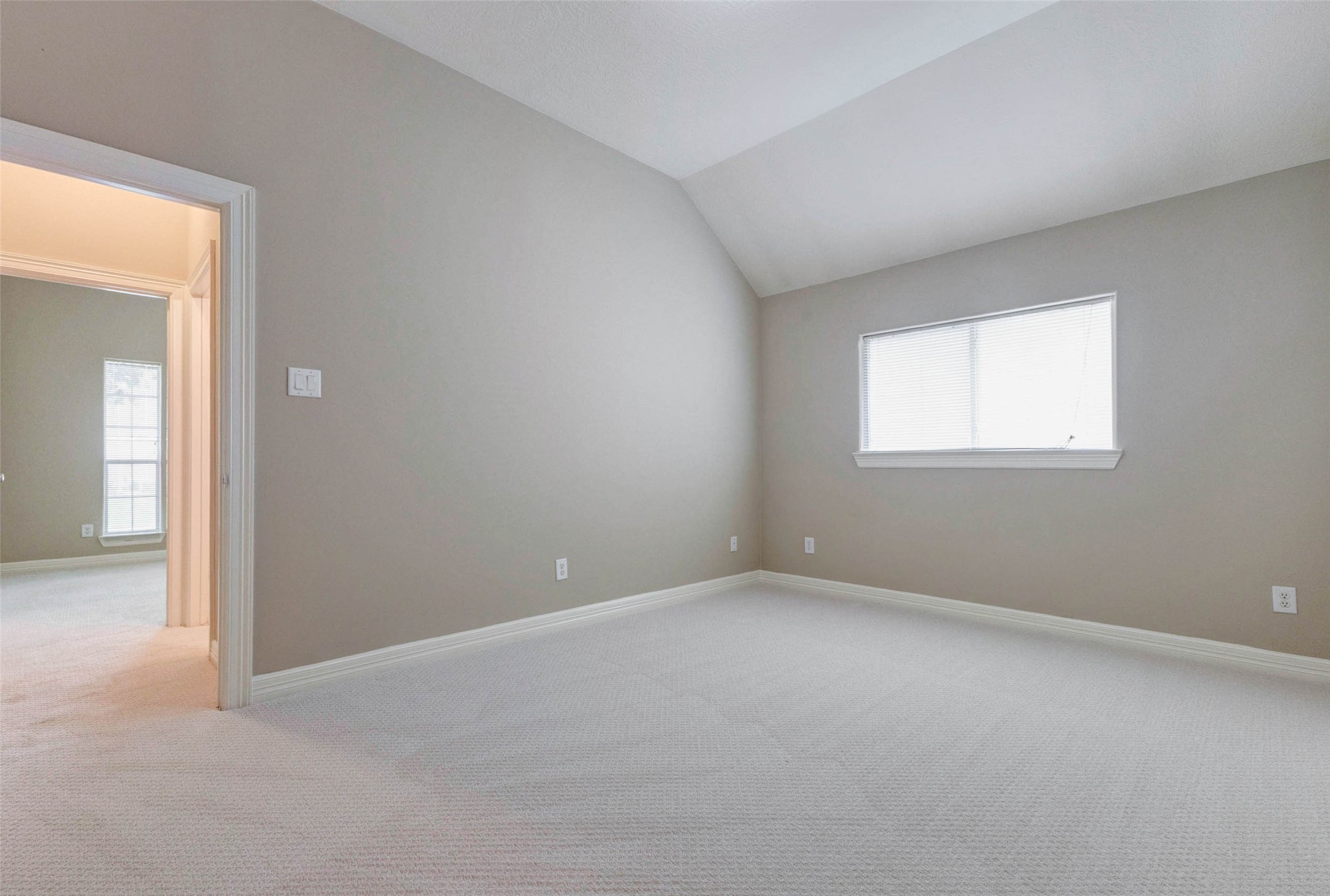 2718 Ridgeglen Lane Houston, TX 77082 - Photo 15 of 26 Bedroom view highlighting the vaulted ceiling, neutral wall color, soft carpet and wide window with blinds. The open doorway shows the connection to the adjacent hall or bedroom area, giving the space a comfortable sense of flow. With ample wall space, natural light and a simple rectangular layout, this room is well suited for sleeping, working, studying or creating a quiet retreat.
