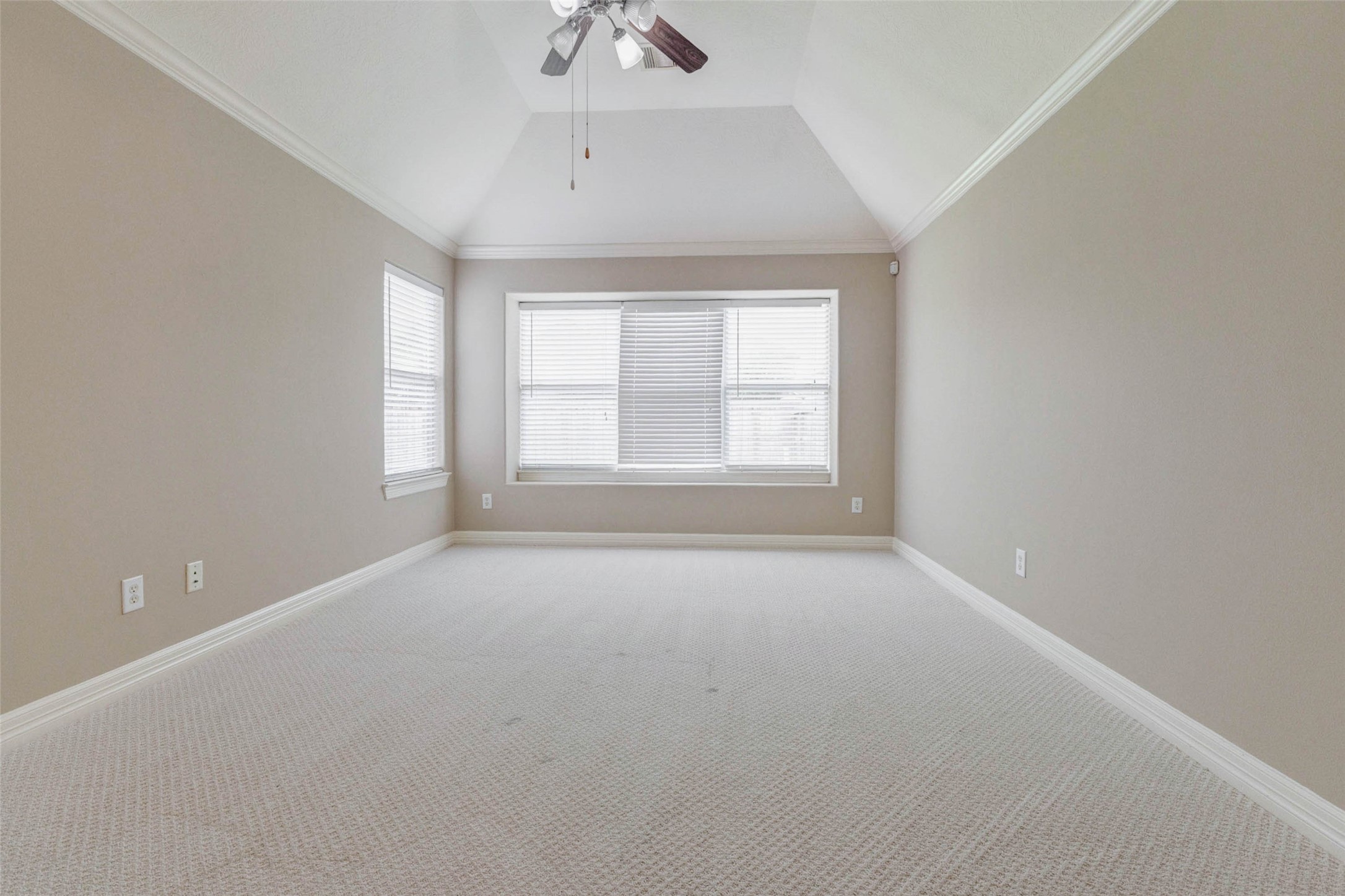 2718 Ridgeglen Lane Houston, TX 77082 - Photo 17 of 26 Wide bedroom view with vaulted ceiling, ceiling fan, crown molding and a large window centered at the end of the room. The long, open layout offers excellent flexibility for bedroom furniture, seating or a home office corner. Light carpet, neutral paint and crisp white trim create a bright foundation, while the ceiling height enhances the overall sense of space and comfort.