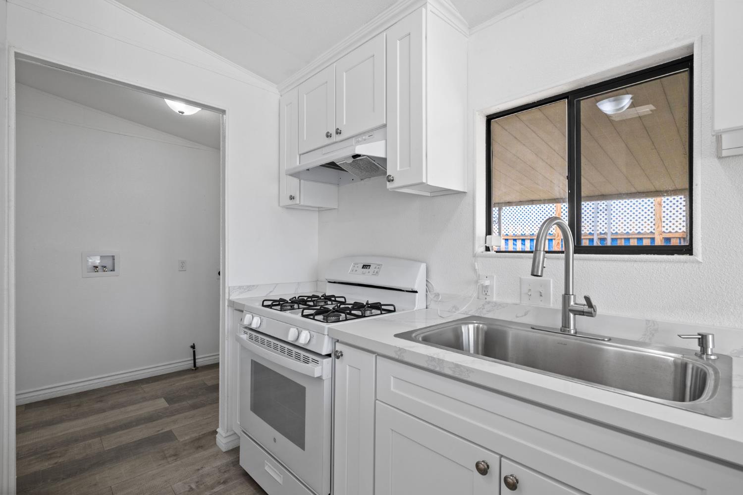 8300 Kern Canyon Road, Unit 156 Bakersfield, CA 93306 - Photo 16 of 40 a kitchen with white cabinets a sink and a stove with wooden floor