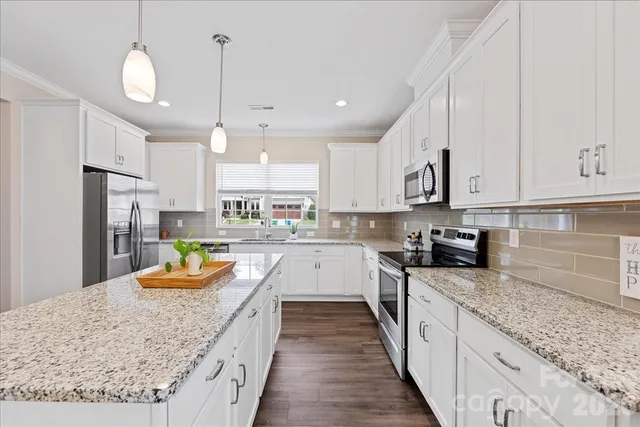 a large kitchen with stainless steel appliances granite countertop a stove top oven a sink a refrigerator and white cabinets