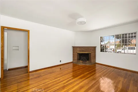 a view of an empty room with wooden floor fireplace and a window