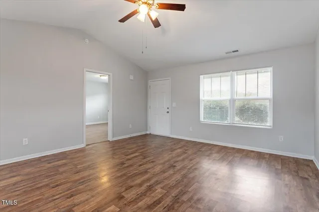 an empty room with wooden floor fan and windows