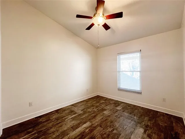 an empty room with wooden floor ceiling fan and windows