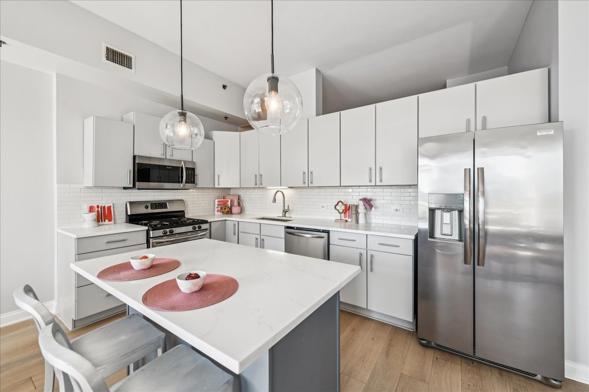 230 West Division Street, Unit 1202 Chicago, IL 60610 - Photo 7 of 20 a kitchen with stainless steel appliances granite countertop a refrigerator a sink dishwasher a stove and white cabinets with wooden floor