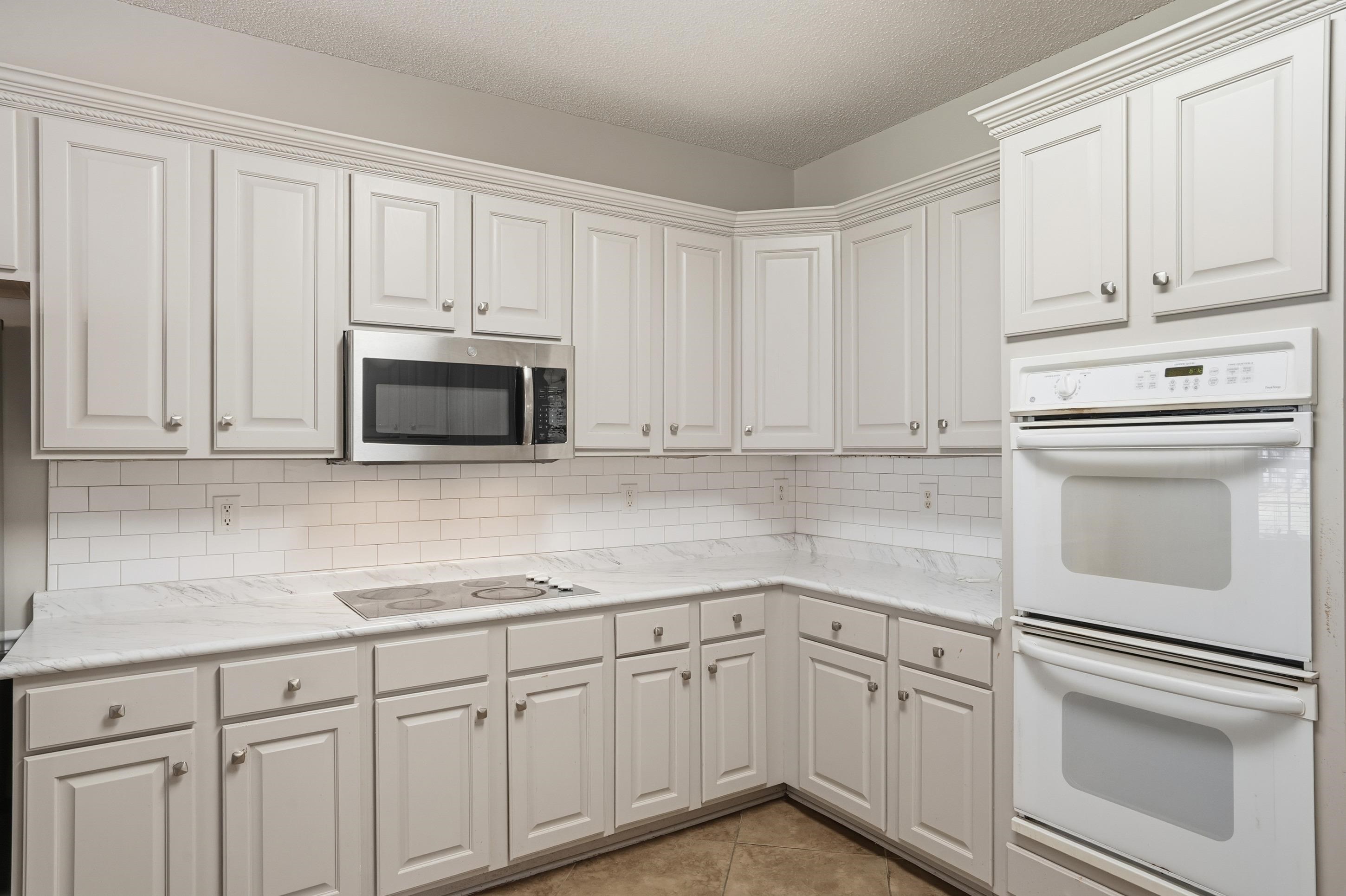 8570 May Orchard Lane Cordova, TN 38018 - Photo 11 of 35 Kitchen featuring white double oven, stainless steel microwave, tasteful backsplash, white cabinets, and a textured ceiling