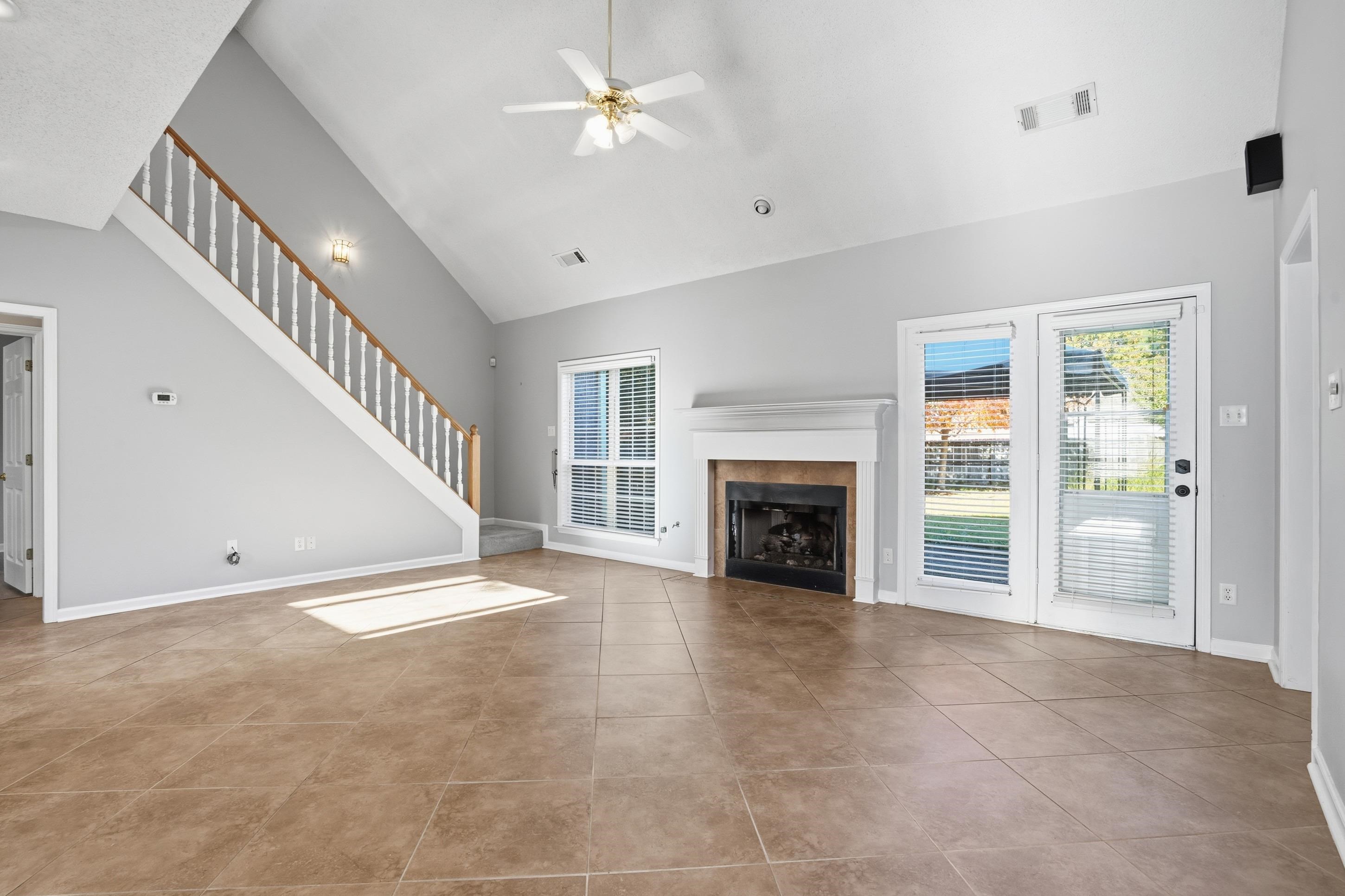 8570 May Orchard Lane Cordova, TN 38018 - Photo 8 of 35 Unfurnished living room featuring a tiled fireplace, plenty of natural light, ceiling fan, stairway, and high vaulted ceiling