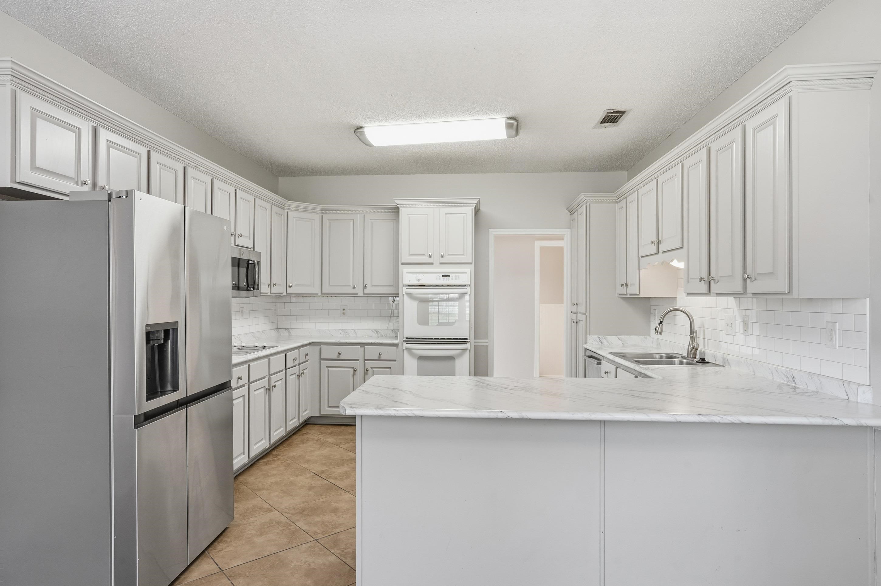 8570 May Orchard Lane Cordova, TN 38018 - Photo 10 of 35 Kitchen with stainless steel appliances, a peninsula, light tile patterned floors, white cabinetry, and decorative backsplash