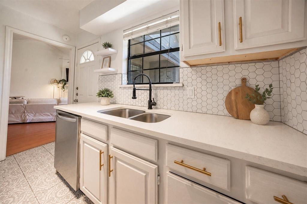 2835 Keller Springs Road, Unit 808 Carrollton, TX 75006 - Photo 4 of 16 Kitchen featuring white cabinetry with gold-toned hardware, a double basin stainless steel sink with a matte black faucet, and a hexagonal tile backsplash